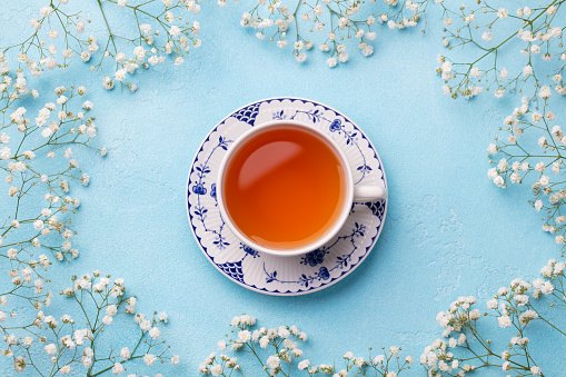 Cup of tea with fresh flowers on blue background. Top view. Copy space