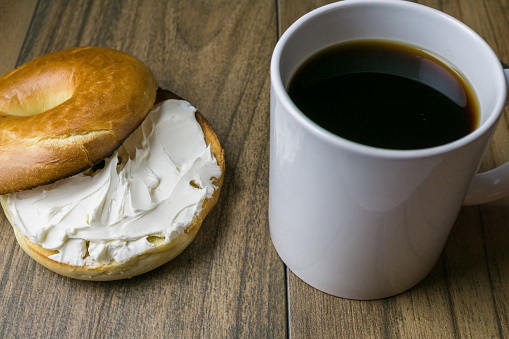 Front view, close up of bagel with coffee, newspaper, cream cheese and brown sugar