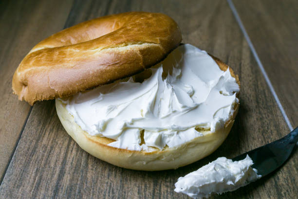 Bagel with cream cheese spread Front view, close up of bagel with cream cheese and spreading knife cream cheese photos stock pictures, royalty-free photos & images