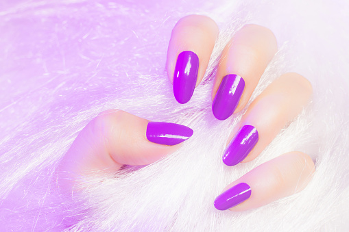 Female hand with pink nails is in white fur texture, manicure and nail care concept.