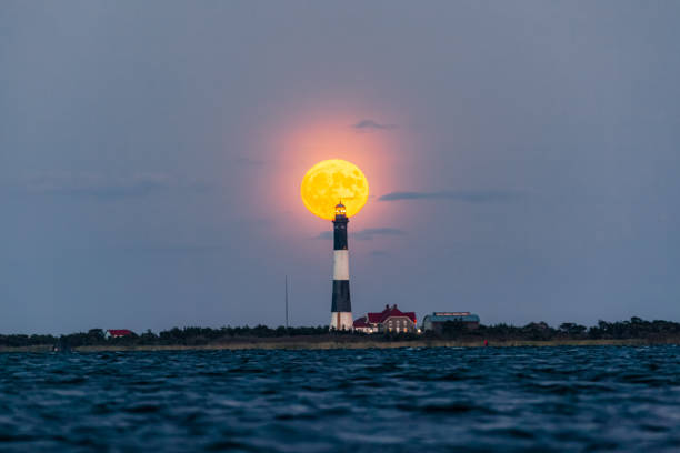 istock Full moon rising behind a tall lighthouse on the coast. 1174688617