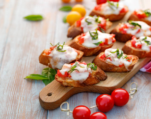 토스트, 토마토를 곁들인 브루스케타, 모짜렐라 치즈, 신선한 바질이 나무 테이블 위에 도마 위에 올려진다. - mozzarella tomato antipasto appetizer 뉴스 사진 이미지