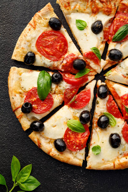 istock Pizza slices with tomatoes, mozzarella cheese, black olives and fresh basil on a black background, top view. 1174701047