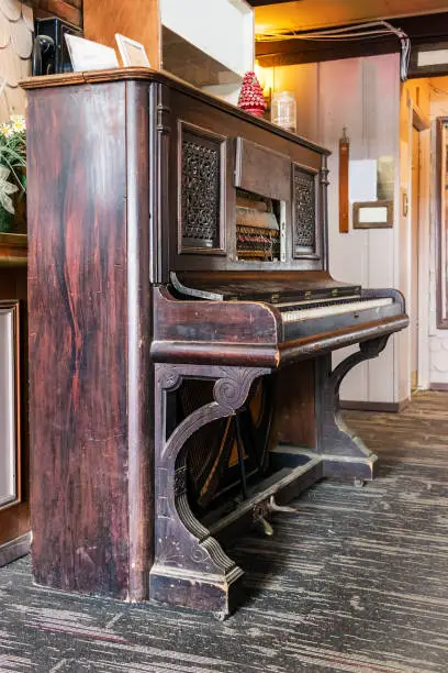 A very old upright acoustic piano on a wooden floor, perspective view.