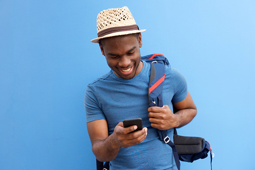 Portrait of cool young african american guy with bag and cellphone against blue background