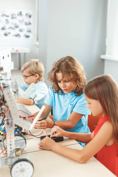 istock Robotics. Children sitting having class making robots welding wires teamwork controlling voltage 1174713134