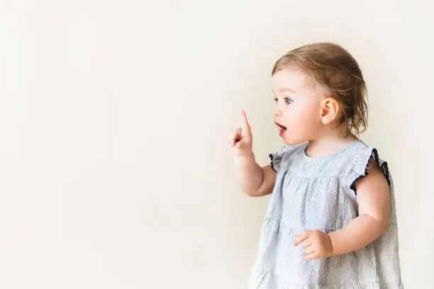 Photo of Baby girl pointing her finger, excited and emotional, on neutral background
