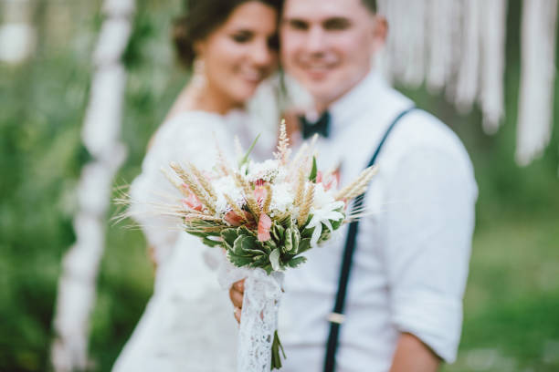 istock Happy newly married couple with boho style bouquet on wedding ceremony in forest. Selective focus on flowers 1174762456