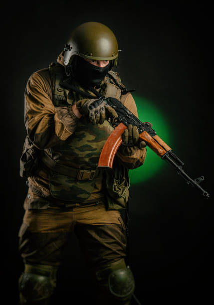 istock a man in uniform with a gun posing, aiming, reloading, shooting, on a dark background in the Studio 1174763492
