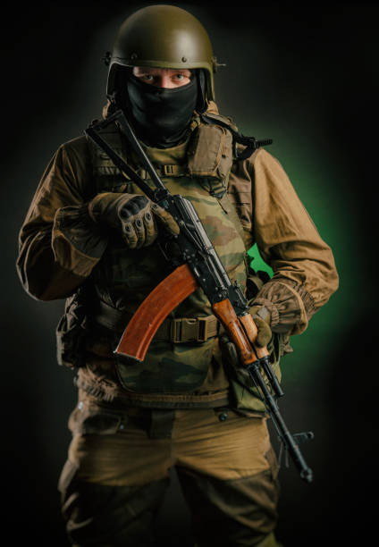 istock a man in uniform with a gun posing, aiming, reloading, shooting, on a dark background in the Studio 1174763494