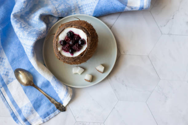 Berry dessert with yogurt in a cup of coconut on a light background. Blackberries, raspberries, blueberries, black currants. Blue napkin
