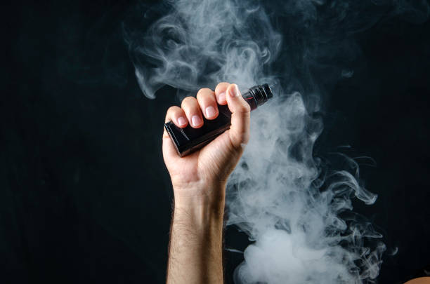 The Evolution of the Electronic Cigarette: A Look Into the Future of Vaping 2 hand holding vape e cigarette or electronic cigarette with white smoke over a black background