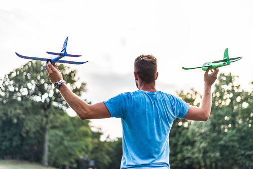 Young man from back, holding two airplane models in nature, on a sunset.