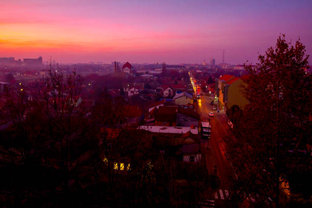 Scenic view on foggy cityscape and asphalt road with vehicles. Colorful sky in sunset.