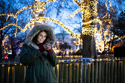 Beautiful woman using smart phone outdoors, by night, in front of christmas decorations.