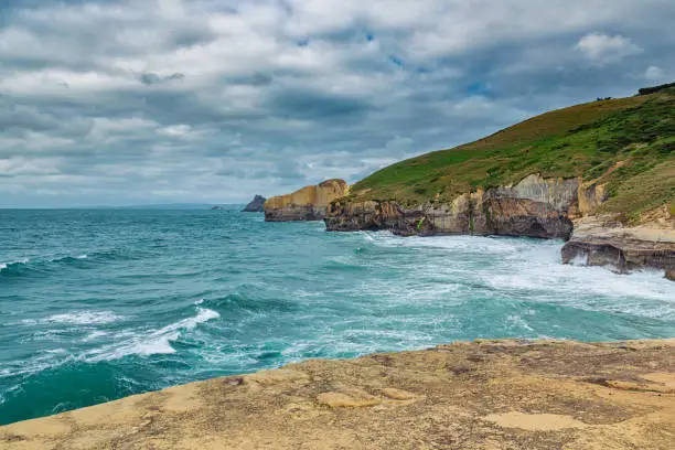 Photo of High sandy cliffs and waves of Pacific ocean at Tunnel beach, New Zealand