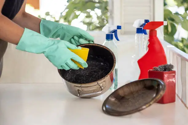 Woman trying to clean burnt pan with chemical cleaners.