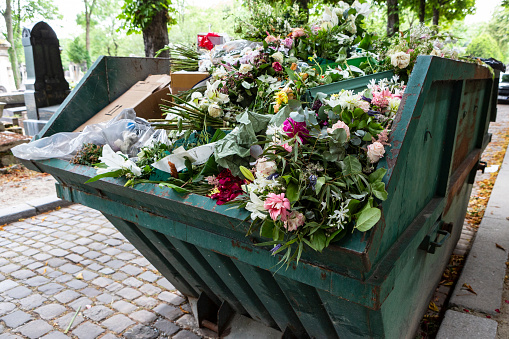 A dumpster filled with discarded flower arrangements that were left behind on graves from visitors at a cemetery.