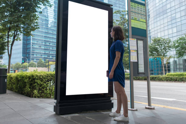 donna in piedi vicino a una lightbox pubblicitaria vuota alla fermata dell'autobus, beffa - esposizione via foto e immagini stock