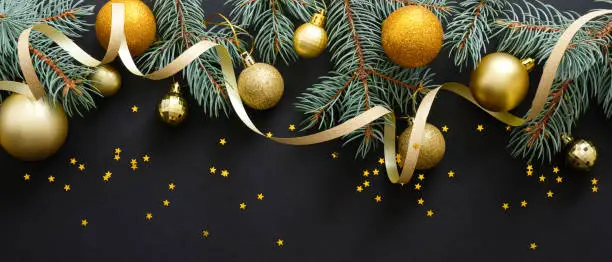 Photo of Black Christmas background with golden decorations, baubles, fir tree branches, confetti. Christmas holiday celebration, winter, New Year concept. Christmas banner mockup, greeting card template.