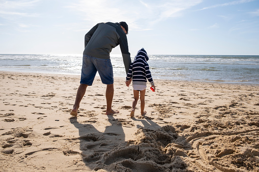 Playful father and son on the beach in cold windy weather in Lacanau Ocean, France. Europe, West Coast.