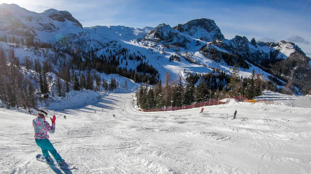 Nassfeld - A snowboarding girl going down the slope A snowboarder going down the slope in Nassfeld, Austria. Perfectly groomed slopes. High mountains surrounding the woman wearing blue trousers and colorful jacket. Girl wears helm for the protection. snowboarding snowboard women snow stock pictures, royalty-free photos & images