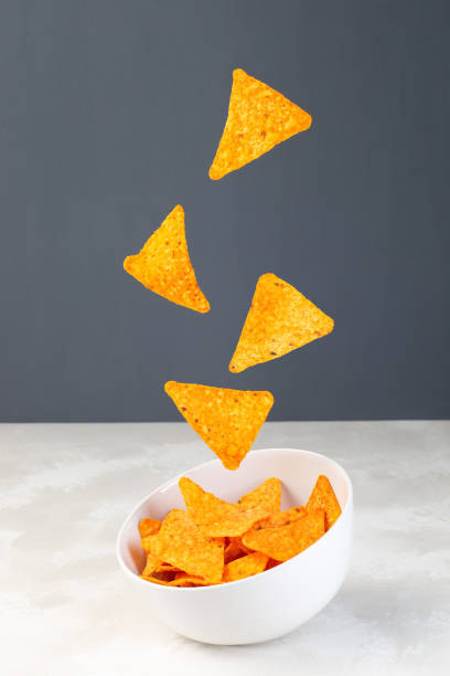 Cheesy tortilla chips or nacho levitate above the bowl,  vertical stock photo