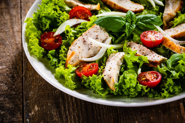 istock Caesar salad  - vegetable salad with roast chicken meat on wooden background 1174831489