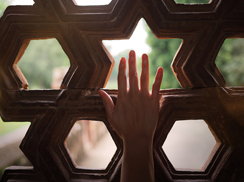 Closeup of a woman hand silhouette reaching out for the sunlight. Background has an Islamic geometrical pattern. Selected focus.