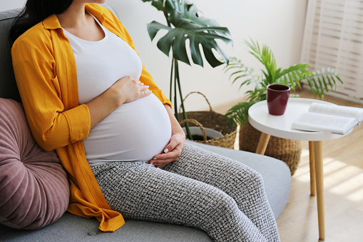 Cropped shot of young beautiful woman on third trimester of pregnancy. Close up of pregnant female with arms on her round belly. Expecting a child concept. Background, copy space.
