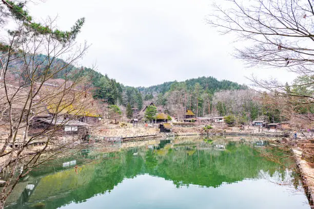 Wooden house buildings in traditional Hida no Sato old folk village near Takayama, Japan by green water pond lake in early spring