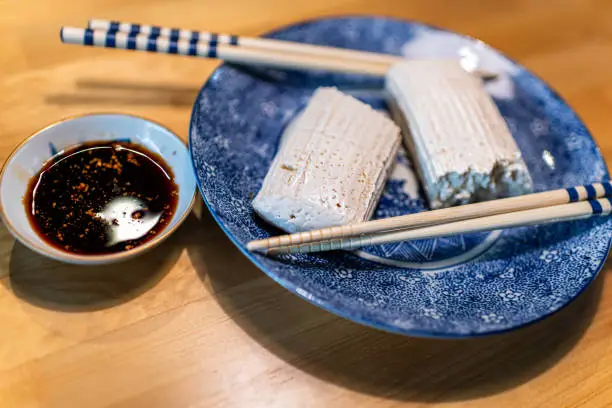 Side view of Japanese traditional komo tofu dofu food, chopsticks and soy sauce on plate on kitchen wooden table in Takayama, Hida in Gifu prefecture