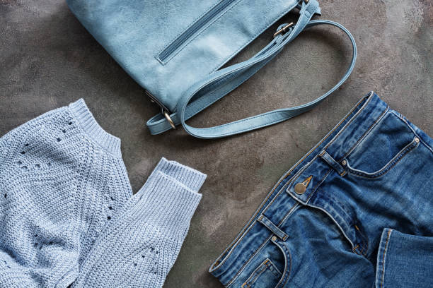 istock Blue jeans, a blue knitted sweater and a leather blue bag on a dark rustic background. Flat lay women's autumn and winter clothes. Stylish female outfit. View from above. 1174845997