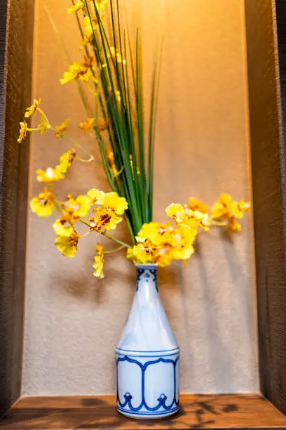 Closeup of traditional Japanese house or ryokan home with yellow flower ikebana in vase decoration decor on wooden shelf in hall