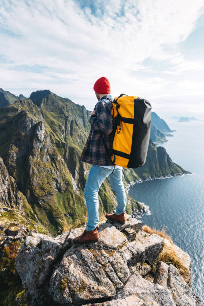 mężczyzna w profesjonalnym plecaku podróżujący samotnie po wysokich górach. podróżnik stojący na skraju klifu skały nad morzem i cieszący się epickim widokiem - rock norway courage mountain zdjęcia i obrazy z banku zdjęć