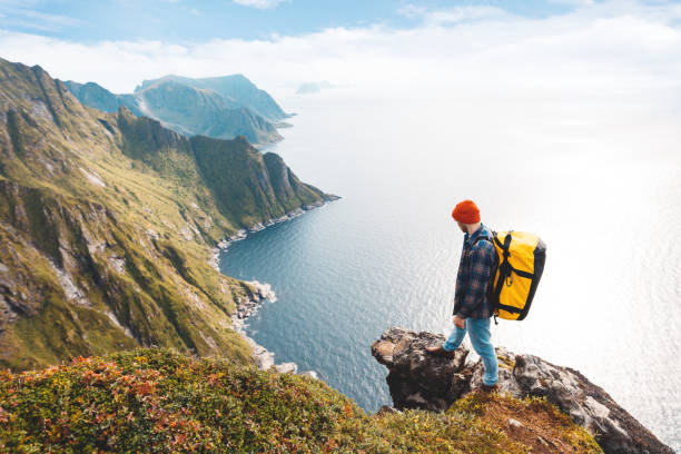 profesjonalny sam expeditor sobie plecak i czerwony kapelusz stojący na krawędzi góry klifu. ekstremalny turysta na wysokiej skale nad morzem. lifstyle i wanderlust - rock norway courage mountain zdjęcia i obrazy z banku zdjęć