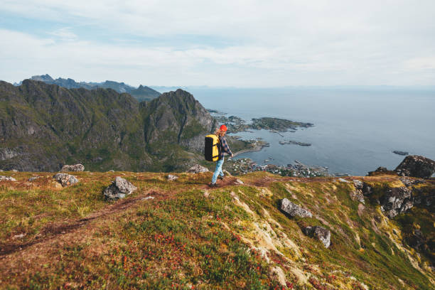 samotny profesjonalny podróżnik z plecakiem na wysokiej górze stojący na skraju klifu i patrzący w przyszłość. przygodowe wakacje w stylu życia - rock norway courage mountain zdjęcia i obrazy z banku zdjęć