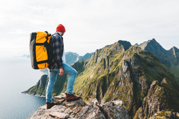 podróżnik ubrany w plecak i czerwony kapelusz wspina się po wysokich górach nad morzem. profesjonalny expeditor stojący na skraju klifu i z niecierpliwością. wanderlust - rock norway courage mountain zdjęcia i obrazy z banku zdjęć