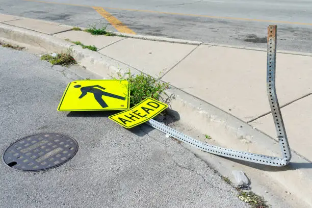 A pedestrian crossing ahead sign knocked down and on the ground in an urban environment