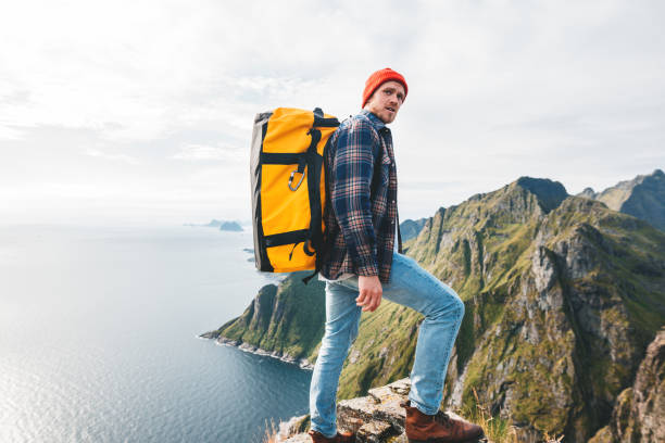 samotny profesjonalny podróżnik z plecakiem na wysokiej górze stojący na skraju klifu i patrzący w przyszłość. przygodowe wakacje w stylu życia - rock norway courage mountain zdjęcia i obrazy z banku zdjęć