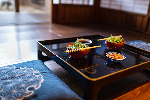 Traditional Japanese restaurant ryokan kaiseki with vegetable dish of boiled salt edamame, natto and soy sauce on plate by chopsticks with shoji sliding paper doors by window