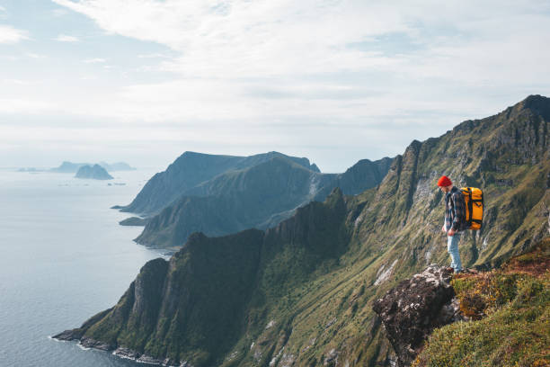 mężczyzna w profesjonalnym plecaku podróżujący samotnie po wysokich górach. podróżnik stojący na skraju klifu skały nad morzem i cieszący się epickim widokiem - rock norway courage mountain zdjęcia i obrazy z banku zdjęć