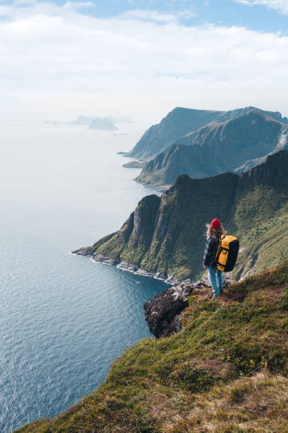 man wearing professional backpack traveling alone on the high mountains. traveler standing on the edge cliff rock above sea and enjoying epic view - rock norway courage mountain imagens e fotografias de stock
