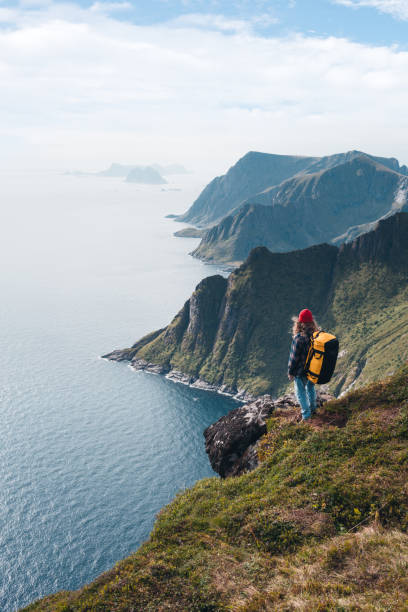 homem que desgasta a trouxa profissional que viaja sozinho nas montanhas elevadas. viajante que está na rocha do penhasco da borda acima do mar e que aprecia a vista épica - rock norway courage mountain - fotografias e filmes do acervo