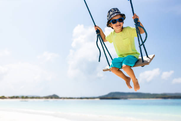 An unrecognisable child swings on a swing at a Park by the Beach in New Zealand's Auckland Region in Summer.