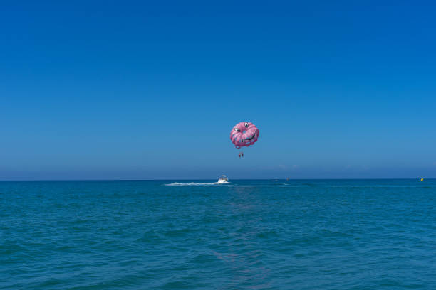 happy couple parasailing on miami beach in summer. couple under parachute hanging mid air. having fun. tropical paradise. positive human emotions, feelings, family, travel, vacation. - florida mid air miami florida people imagens e fotografias de stock