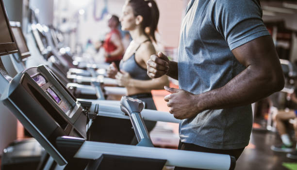 istock Panoramic view of unrecognizable black athlete jogging on treadmill in a gym. 1174852246