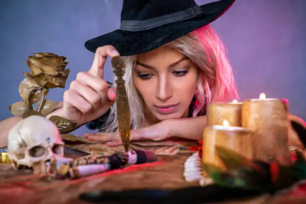 Vodoo girl with knife on table and witch hat with candles and skull