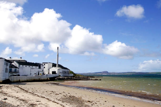 Bowmore distillery and Loch Indaal on Islay Bowmore, Islay, Scotland - May 02 2018: The Bowmore whisky distillery seen from the beach at Loch Indaal on the Isle of Islay. Bowmore is the oldest active distillery on the island. bowmore whisky stock pictures, royalty-free photos & images