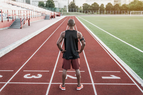 atleta in piedi alla linea di partenza con le mani sulla vita. vista posteriore del corridore in piedi sulla pista da corsa. - sports clothing practicing success vitality foto e immagini stock